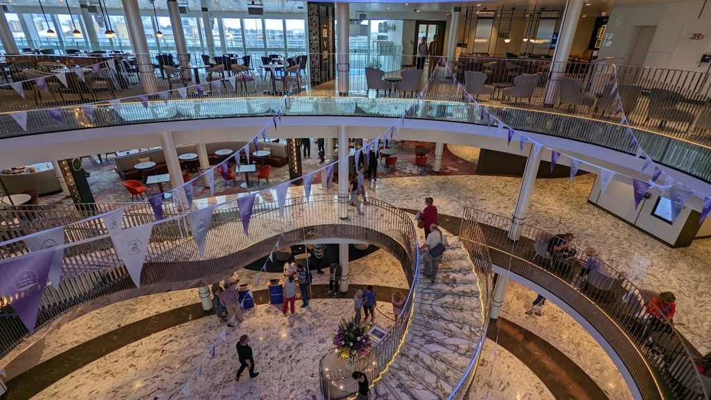 The atrium of P&O Iona with wide staircases and glass walls looking out onto the dockside.