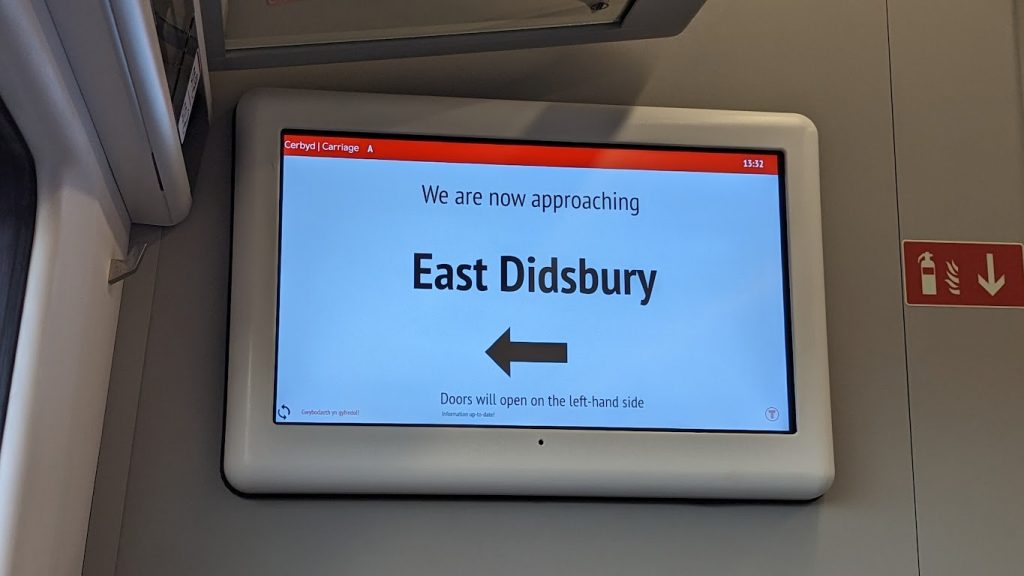 The passenger information screen on Transport for Wales 197008, indicating that passengers wishing to alight at East Didsbury railway station should exist the train on the left-hand side.