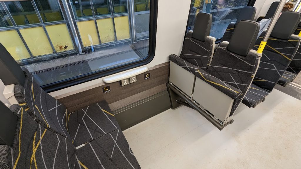 The multi-use space on a class 777 train. There are four seats, two of which have been folded up to create more space.