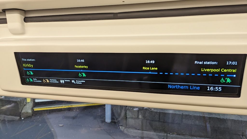 The passenger information screen on a class 777 train, showing the calling points between Kirkby and Liverpool Central. Every stop shown except Rice Land has a green wheelchair and buggy symbol underneath, indicating that the station is fully accessible.